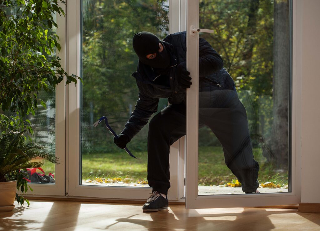 Maskierter Einbrecher versucht durch eine Terrassentür in ein Haus einzudringen.