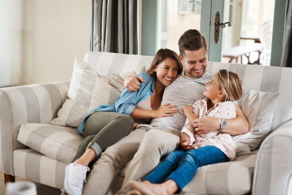 Glückliche Familie sitzt entspannt gemeinsam auf einem Sofa im Wohnzimmer.